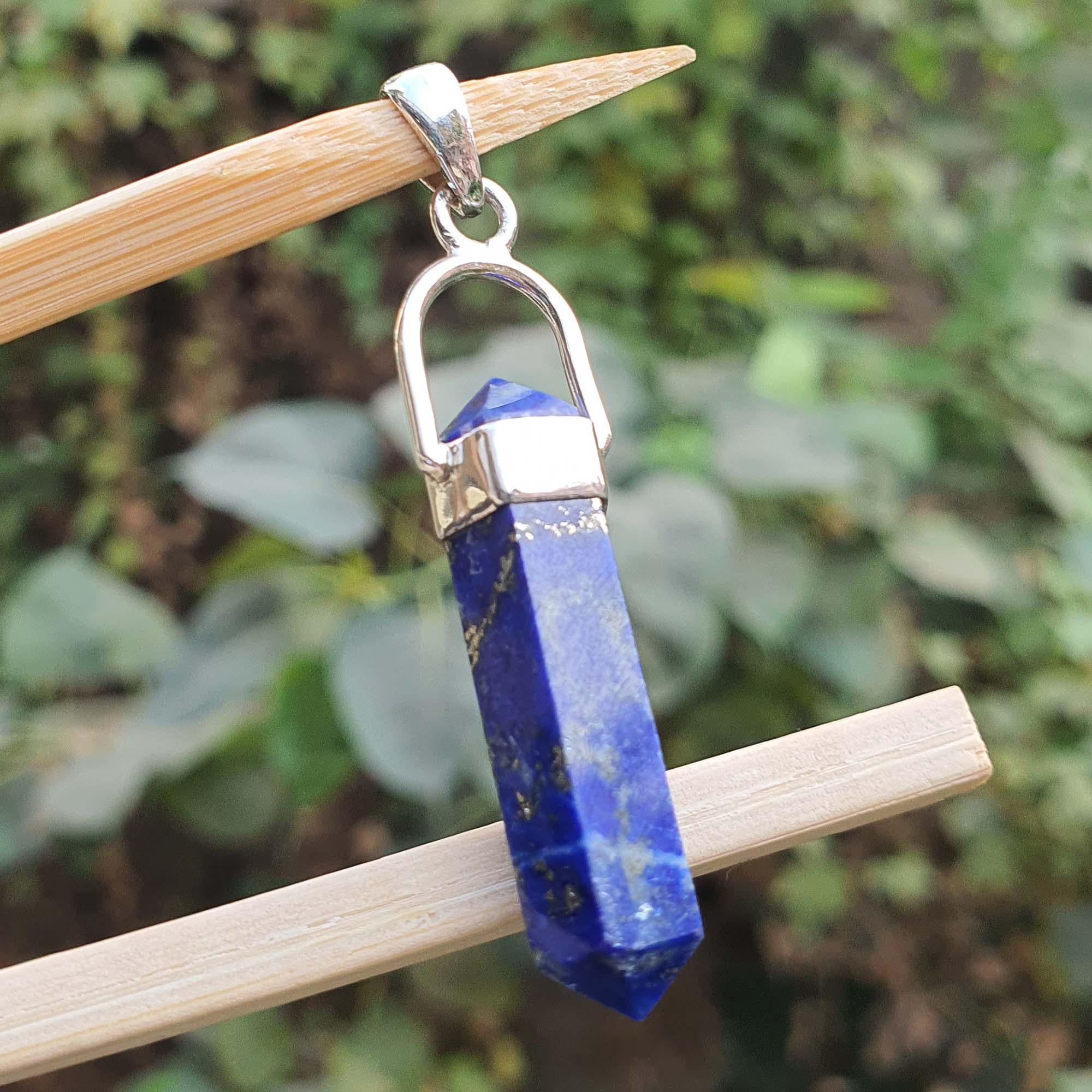 Blue crystal pendant with silver hook on a wooden stick against a green leafy background