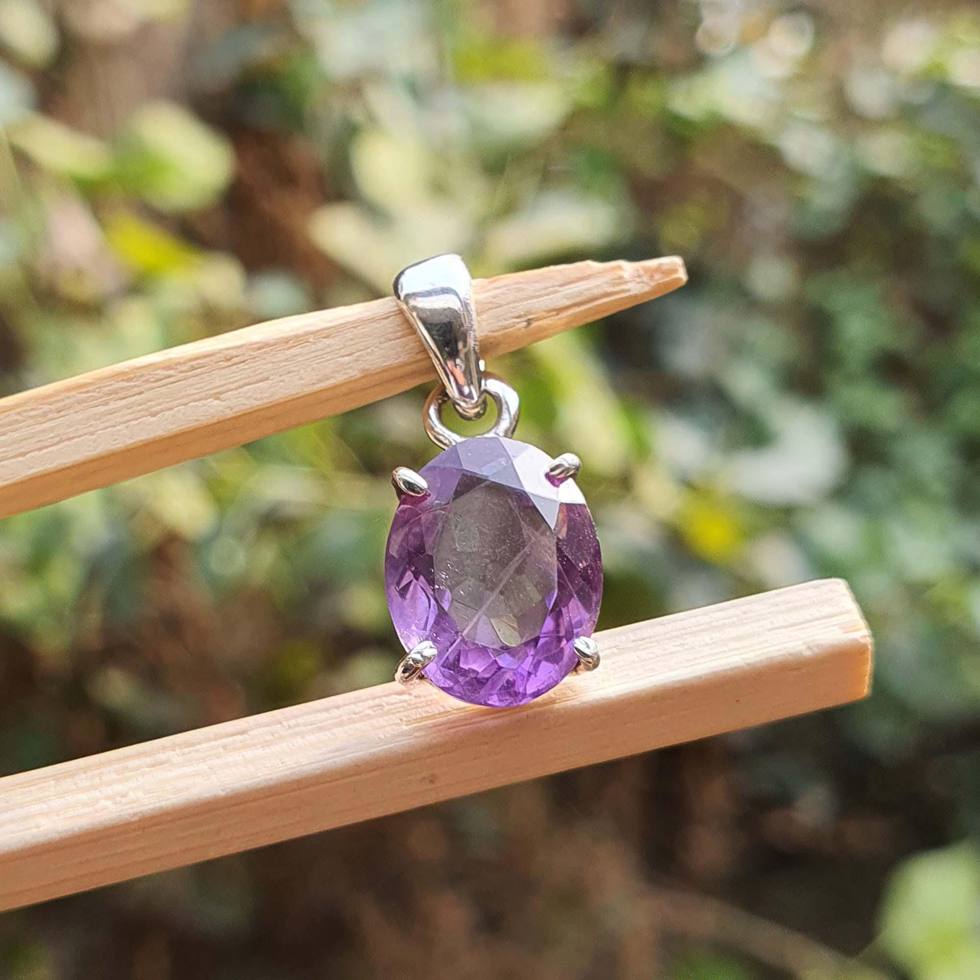 Amethyst pendant on a silver chain held by wooden sticks with a blurred green background