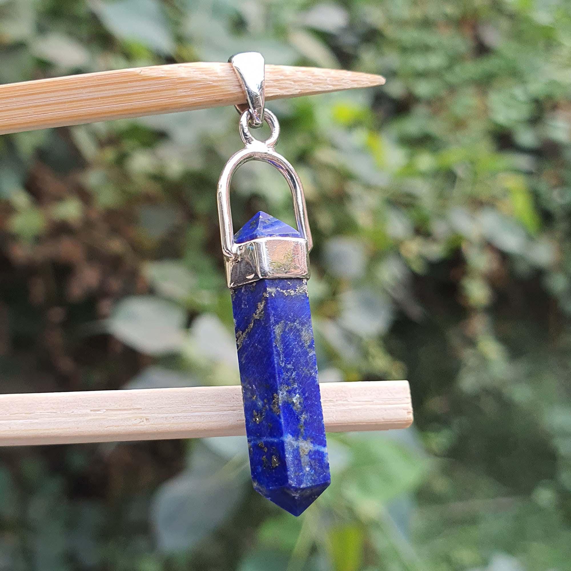 Blue crystal pendant with silver chain on a wooden stick against a blurred green background