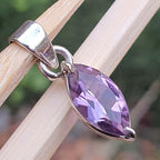 Purple gemstone pendant on a silver chain held by wooden sticks with a blurred natural background