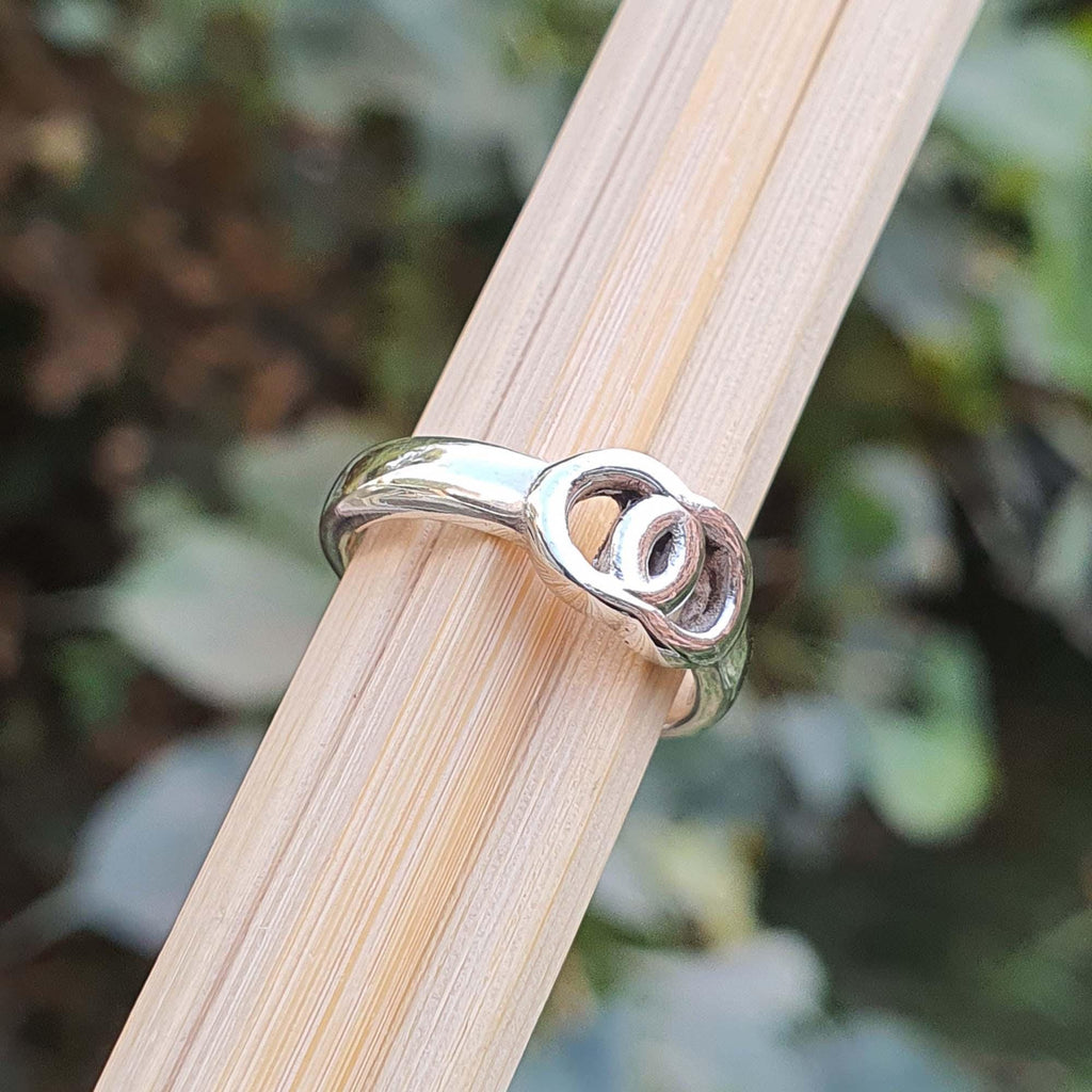 Silver ring with a unique design on a wooden stick against a blurred natural background