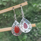 Silver earrings with red teardrop stones on a wooden stick against a blurred green background