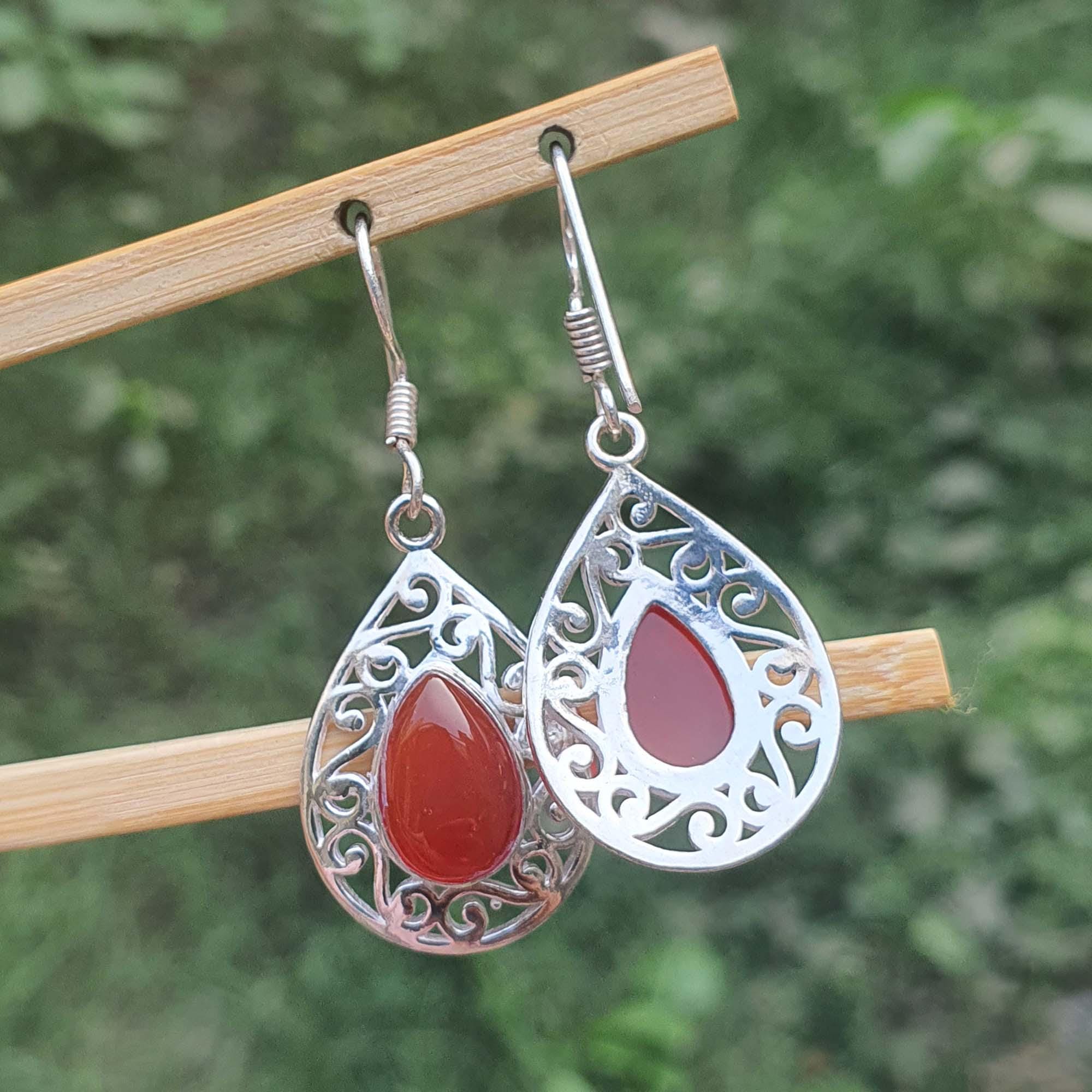 Silver earrings with red teardrop stones on a wooden stick against a blurred green background