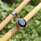 Silver pendant with a dark gemstone on a wooden stick against a blurred green background