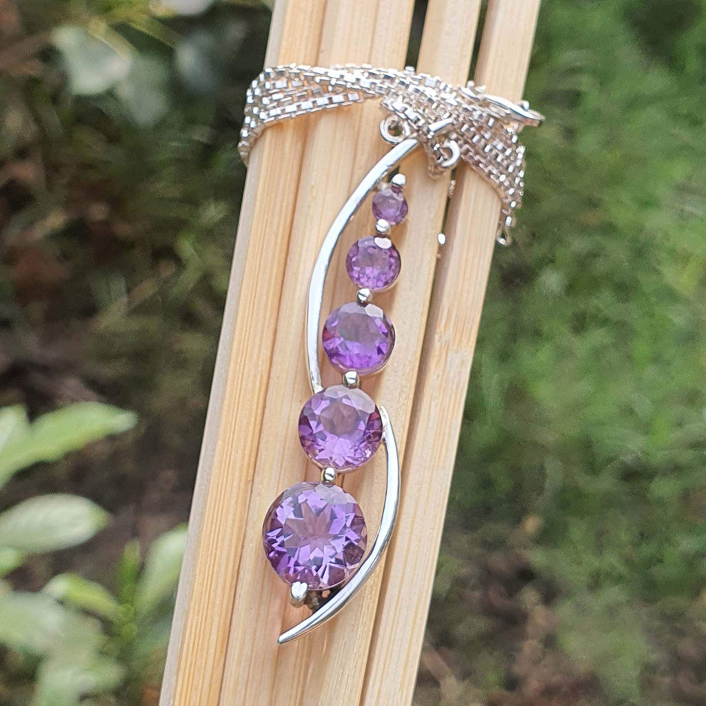 Silver brooch with purple gemstones on a wooden stick against a natural background