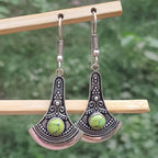 Silver earrings with green stones hanging on a wooden stick against a blurred green background