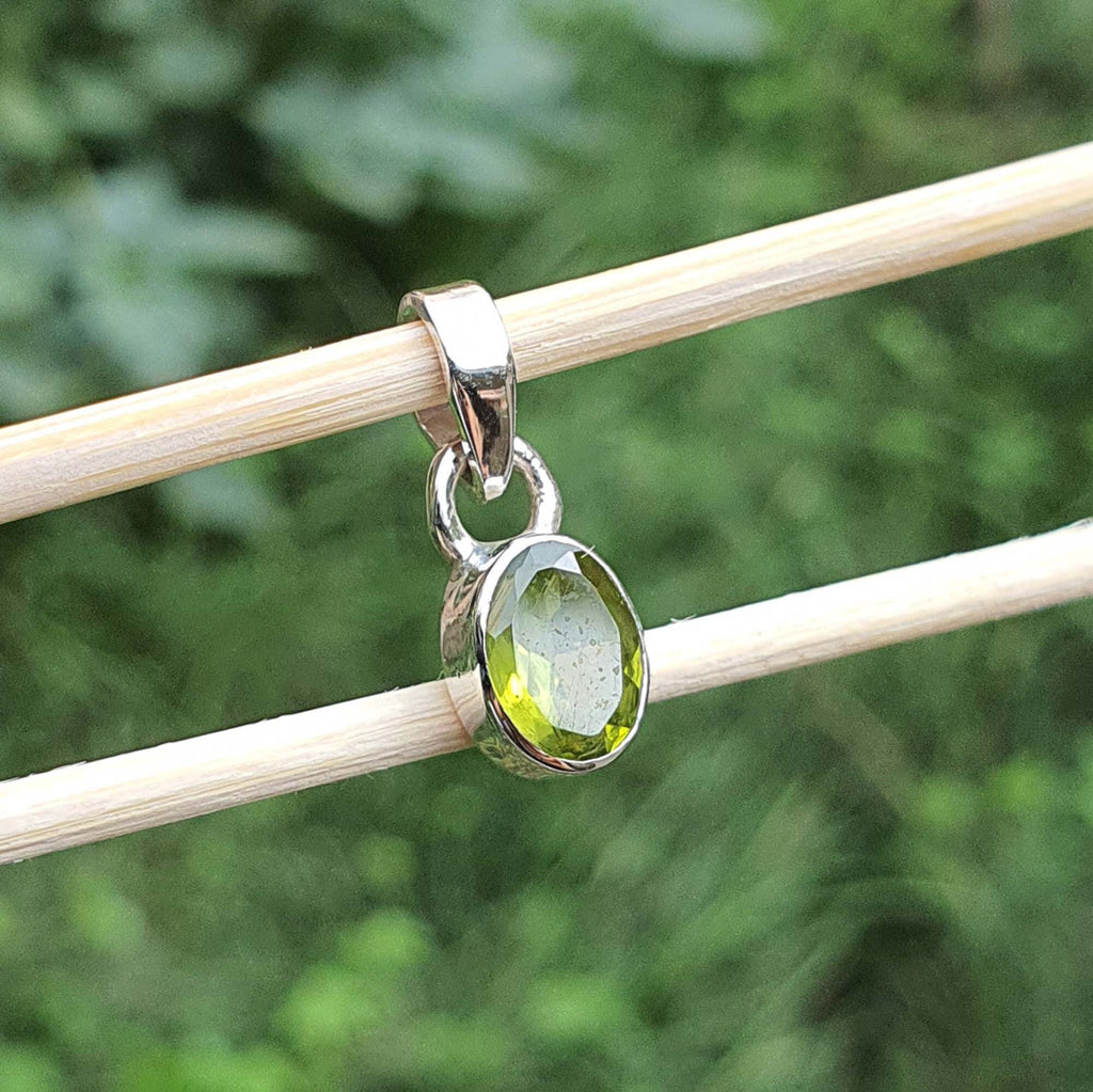Silver pendant with a green gemstone on a stick against a blurred green background
