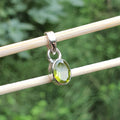 Silver pendant with a green gemstone on a stick against a blurred green background