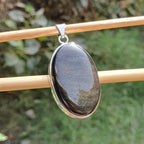 Oval-shaped pendant with a metallic sheen on a blurred natural background