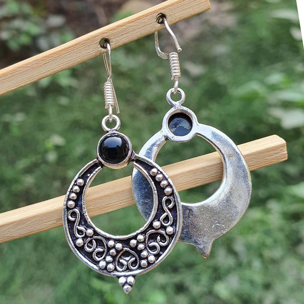 Silver earrings with black stones on a wooden stick against a blurred green background