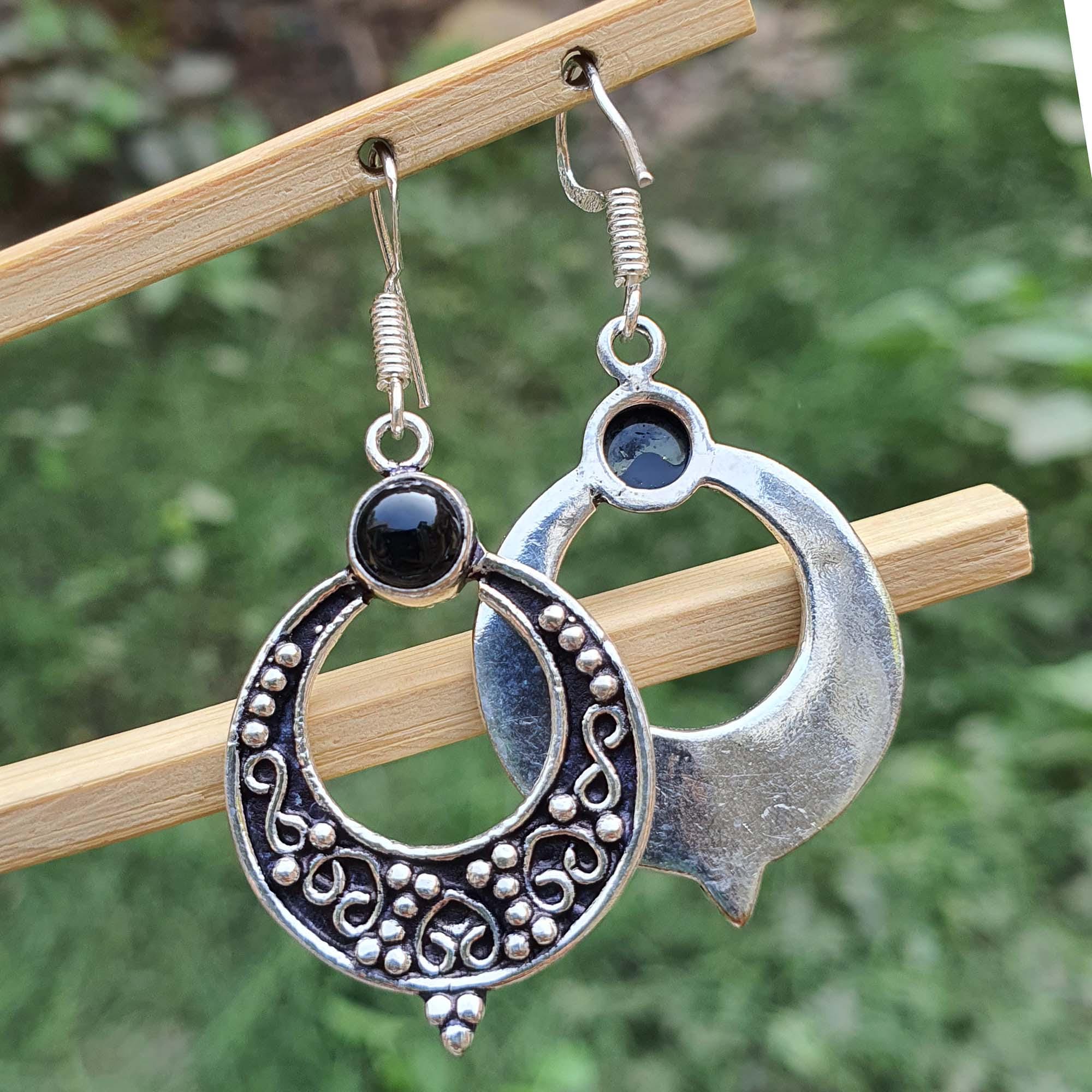 Silver earrings with black stones on a wooden stick against a blurred green background
