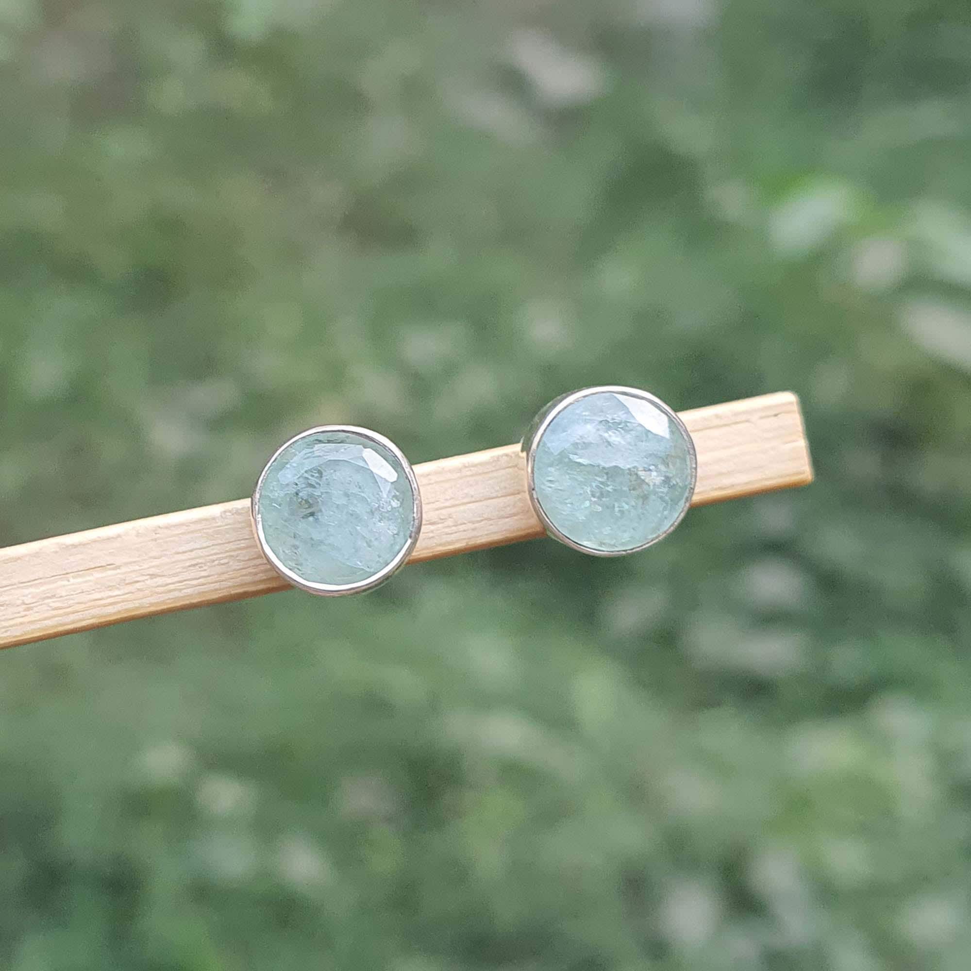 Pair of round earrings with a green gemstone on a wooden stick against a blurred green background
