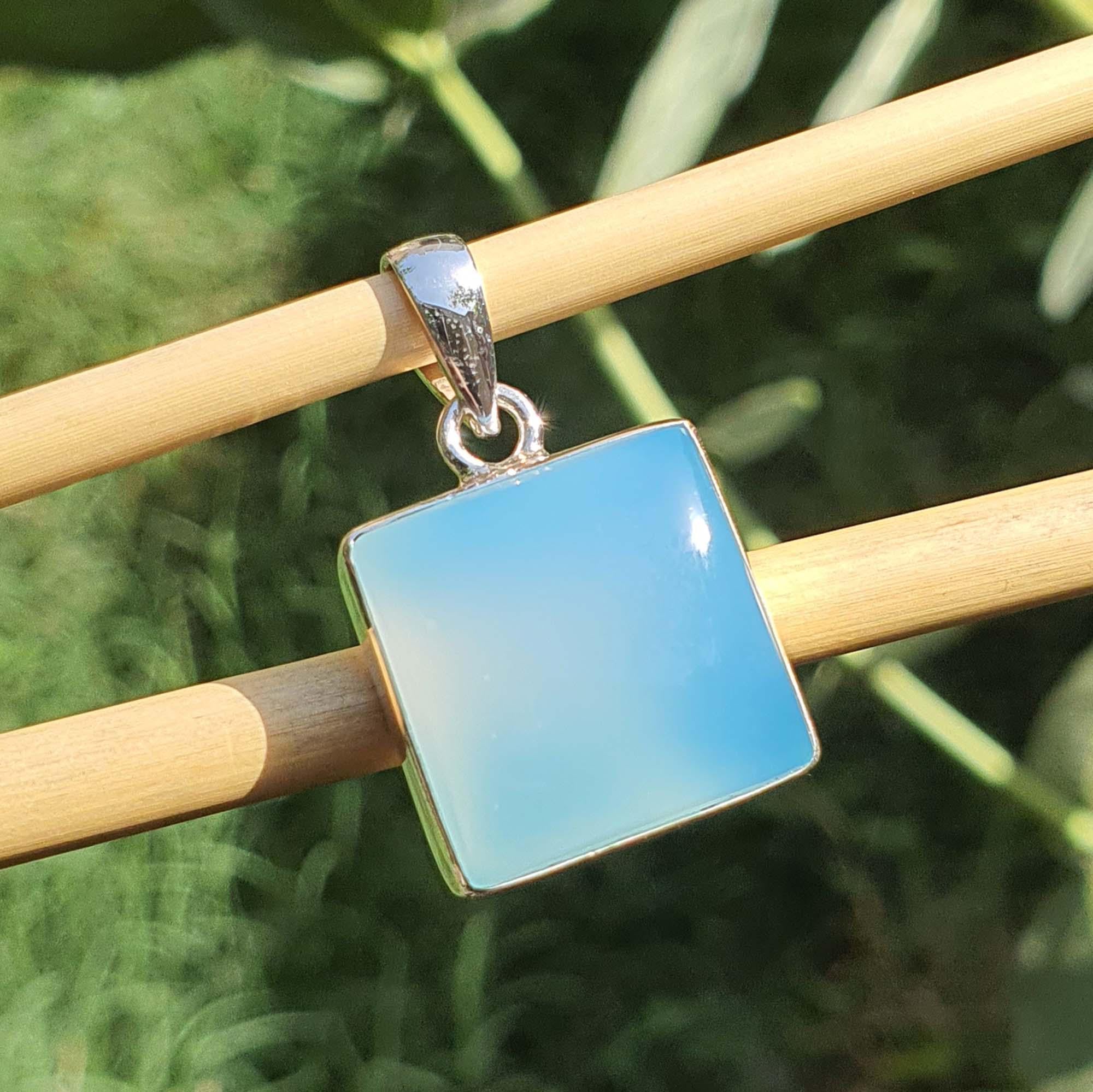Blue square pendant on a silver chain against a green leafy background