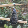 Teardrop-shaped pendant with a textured surface on a wooden stick against a blurred natural background