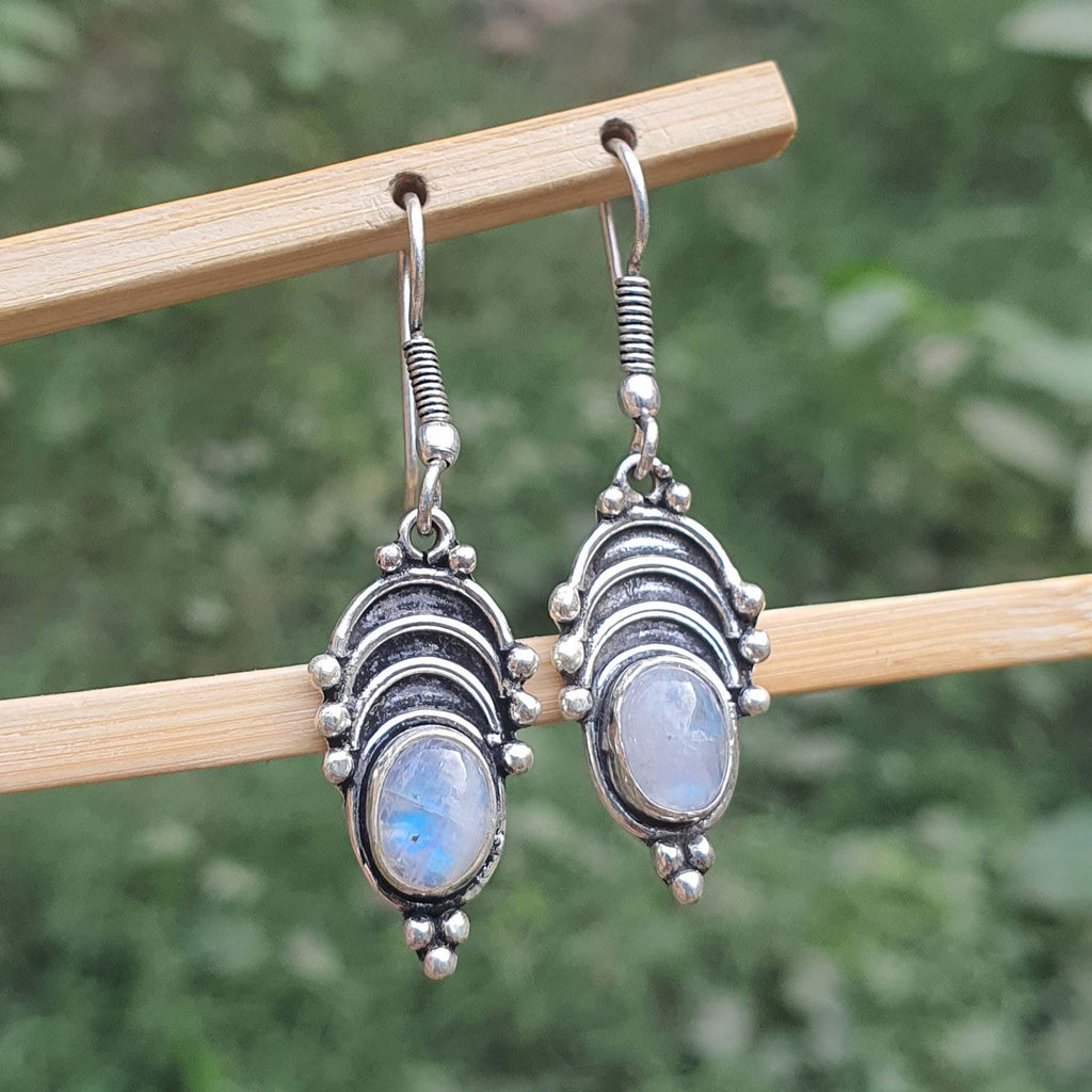 Silver earrings with gemstones on a wooden stick against a blurred green background