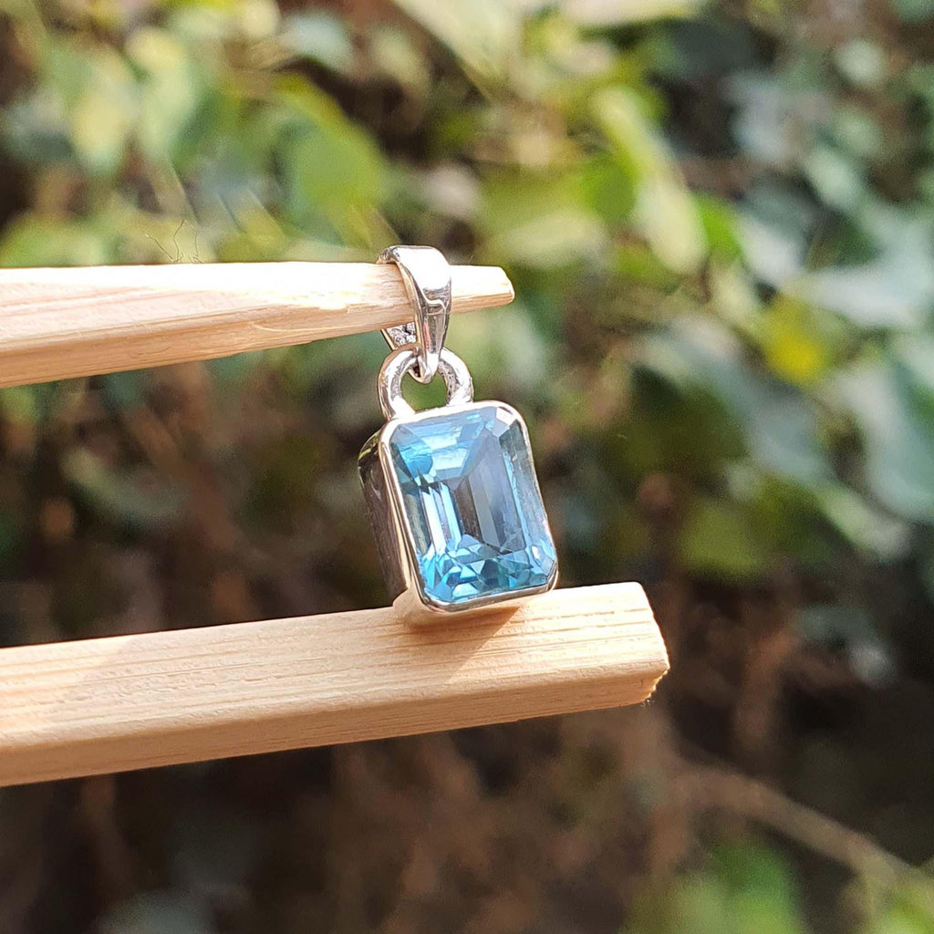 Silver pendant with a blue gemstone on a wooden stick against a blurred green background