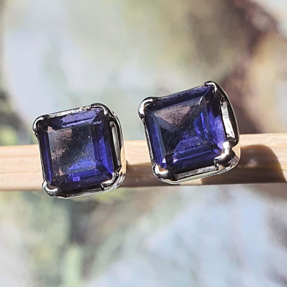 Pair of blue gemstone earrings on a wooden stick with a blurred natural background