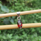 Silver pendant with a red gemstone on a wooden stick against a blurred green background