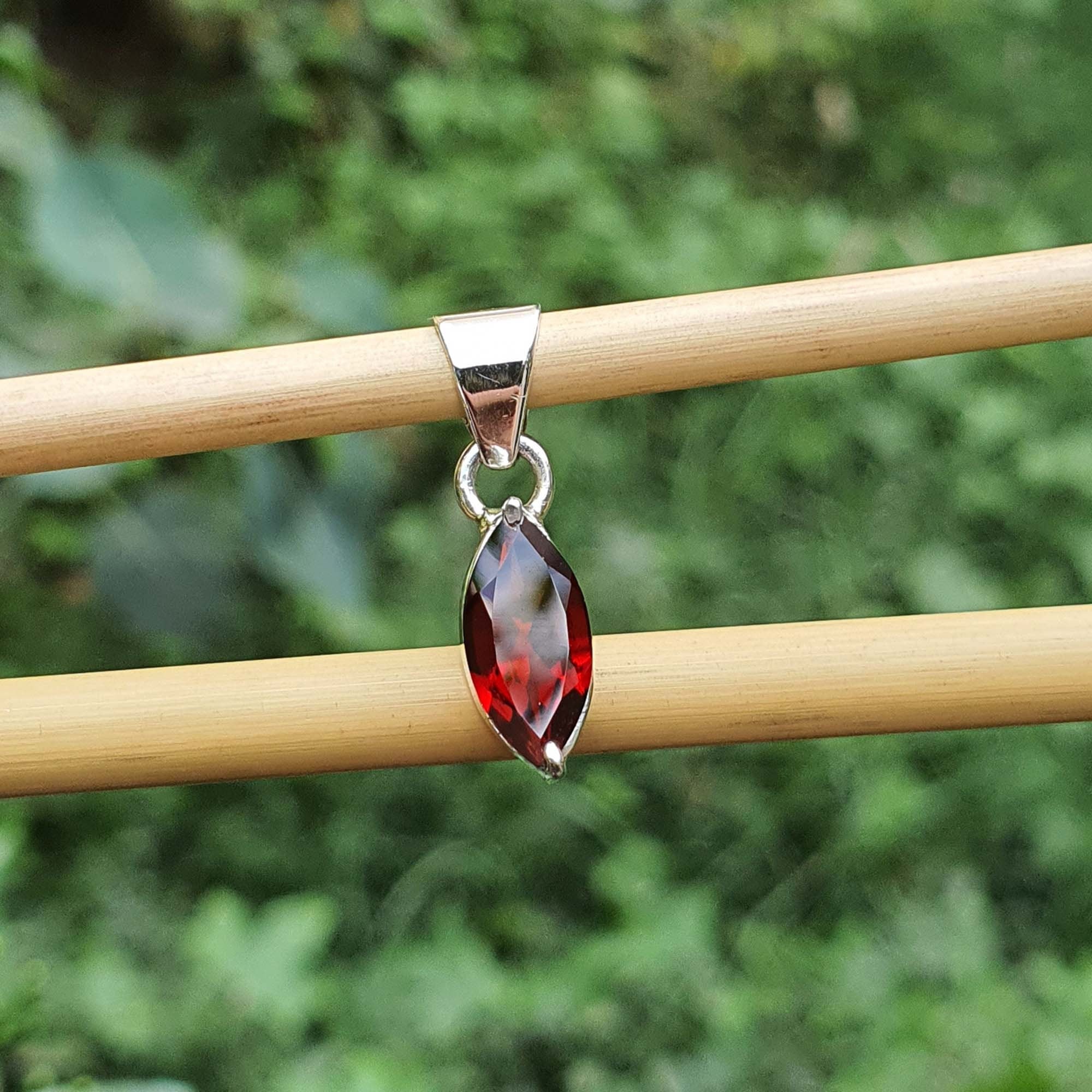 Silver pendant with a red gemstone on a wooden stick against a blurred green background