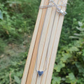 Silver necklace with a heart pendant on a wooden stick against a green leafy background