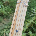 Silver necklace with a heart pendant on a wooden stick against a green leafy background
