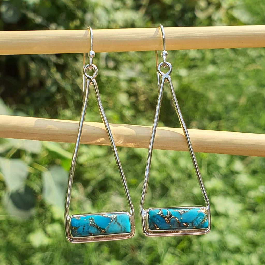 Pair of silver earrings with turquoise stones on a wooden stick against a green foliage background
