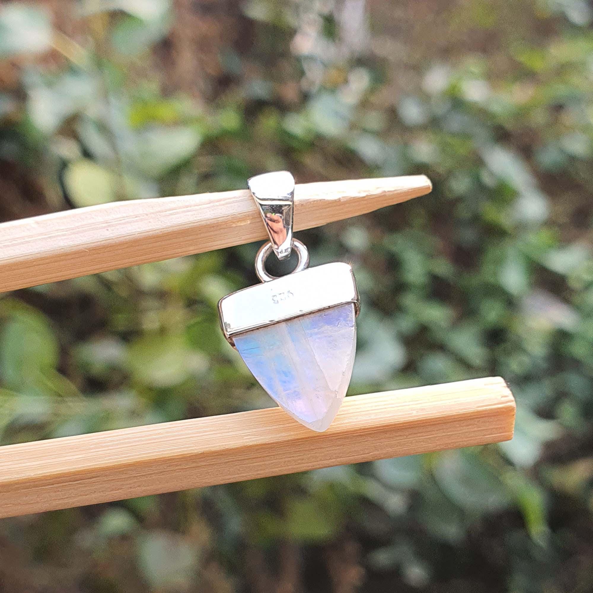 Silver pendant with a rainbow moonstone on a wooden stick against a blurred green background