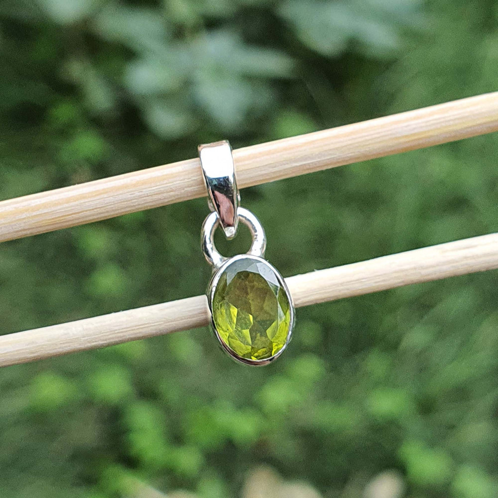 Green gemstone pendant on a silver chain against a blurred green background