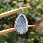 Teardrop-shaped pendant with silver frame on a wooden stick against a blurred green background