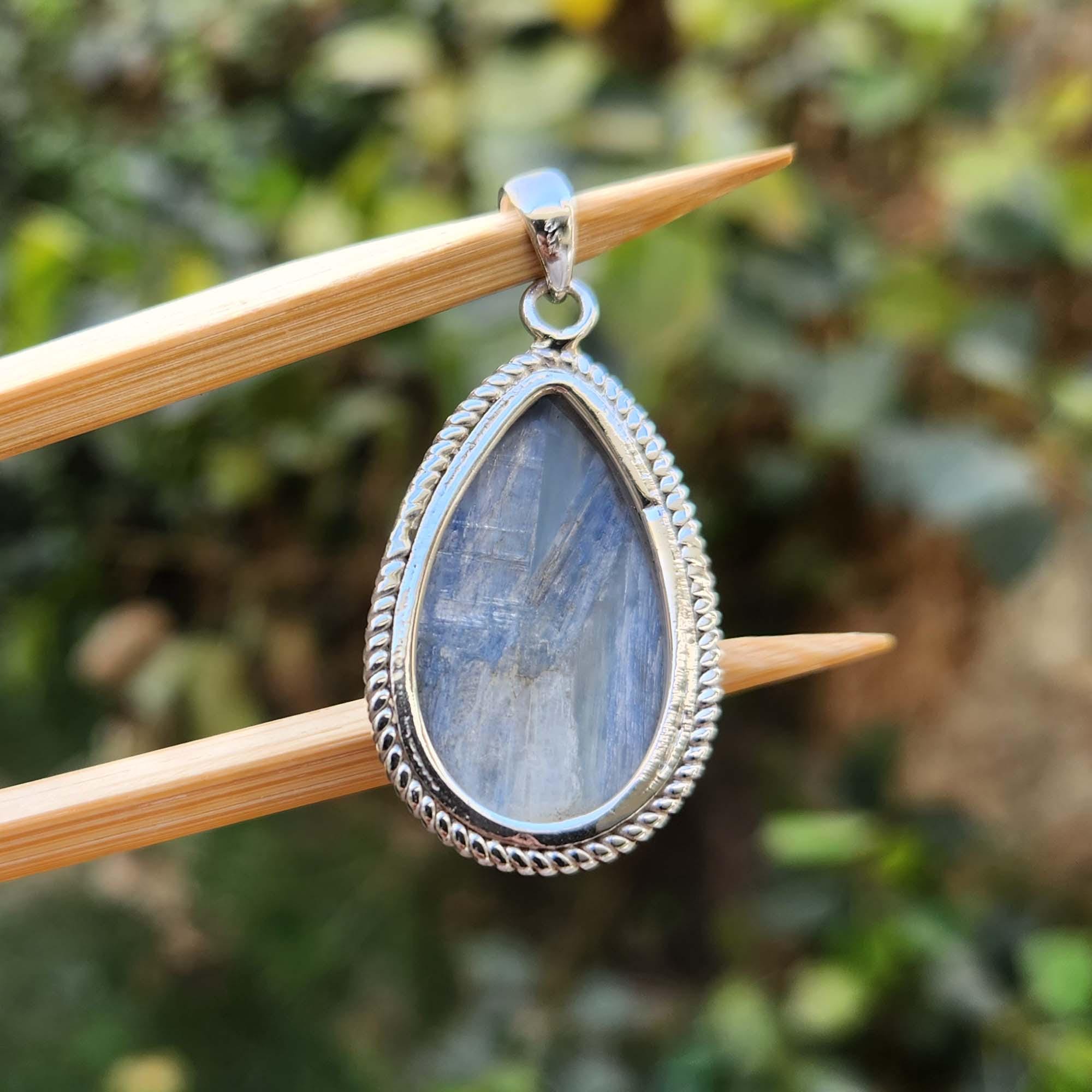 Teardrop-shaped pendant with silver frame on a wooden stick against a blurred green background
