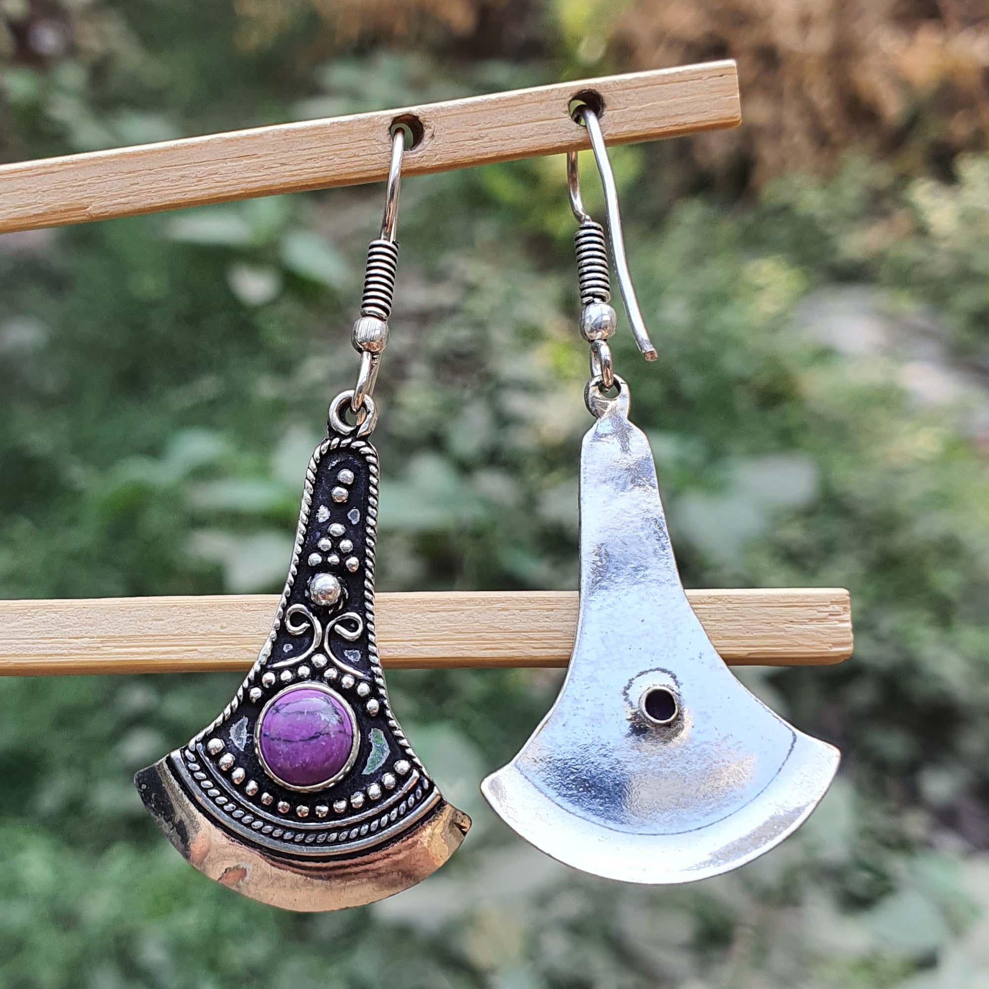 Two unique earrings hanging on a wooden stick with a natural background.