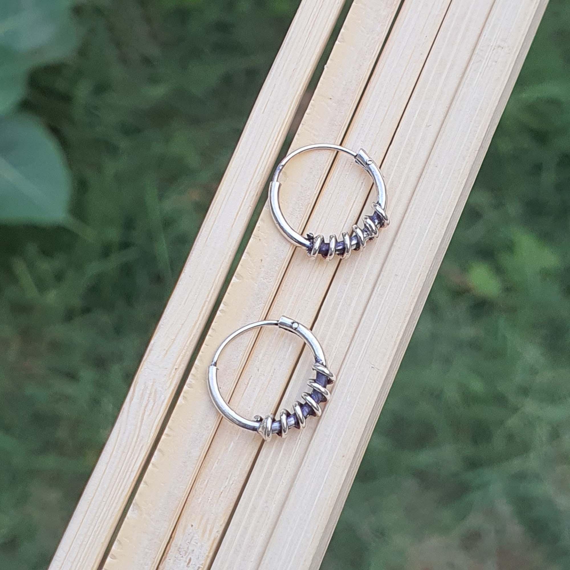 Pair of silver hoop earrings on a wooden surface with a natural background