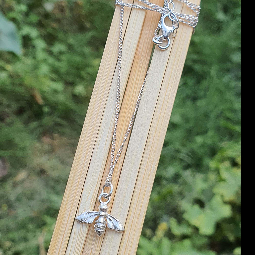 Silver bee pendant necklace on a wooden stand with a natural background