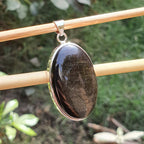 Black stone pendant on gold chain against a natural background