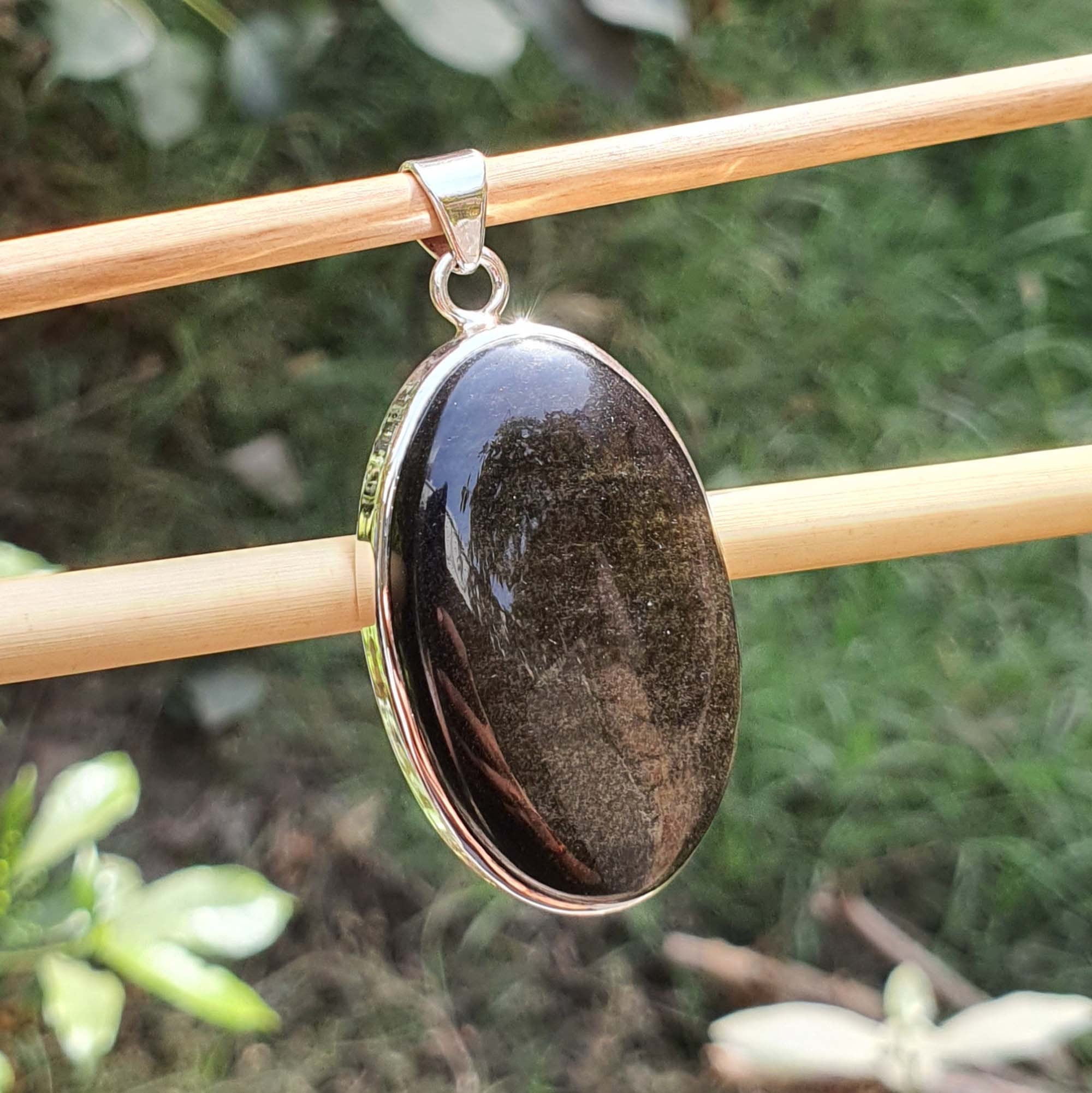 Black stone pendant on gold chain against a natural background