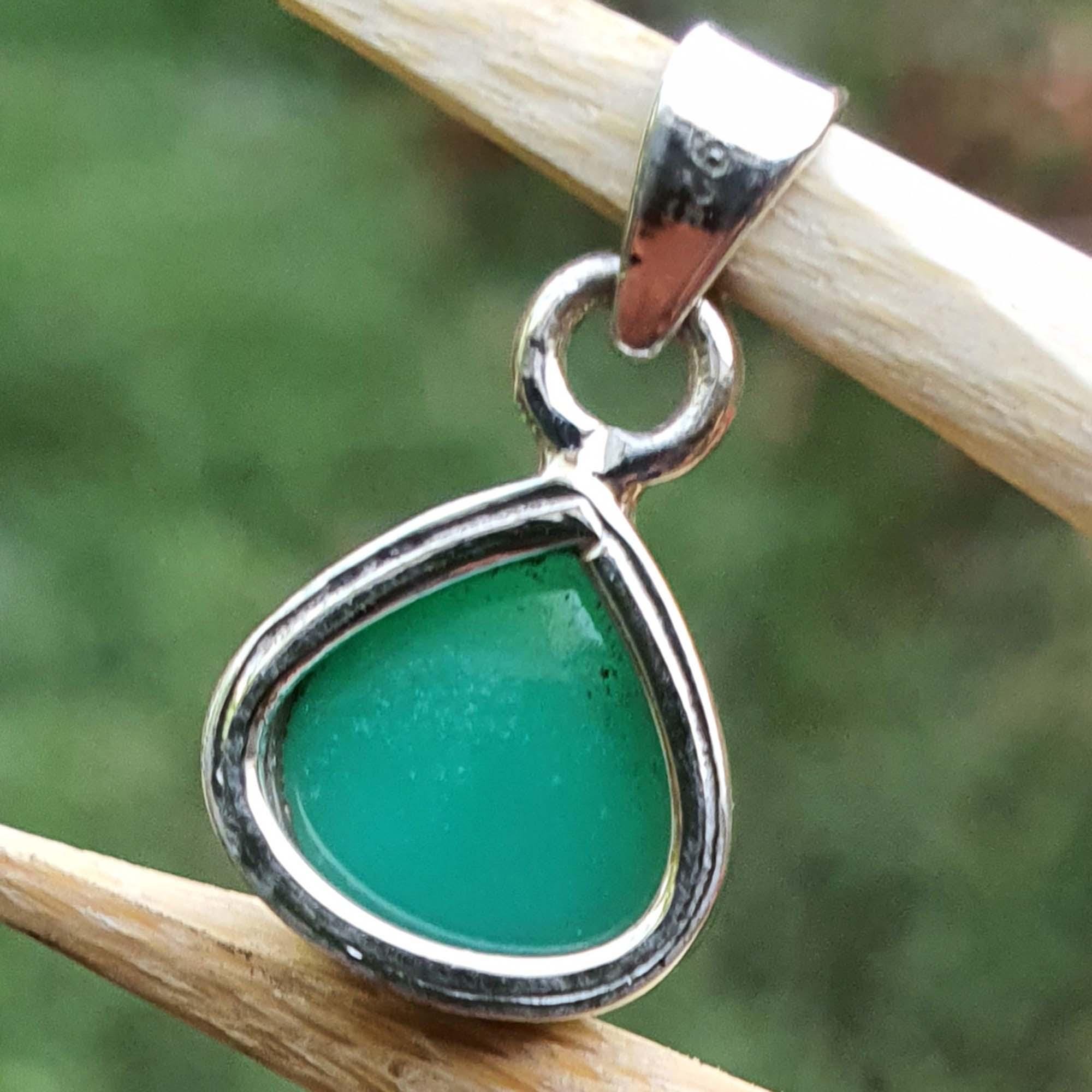 Green teardrop pendant with silver frame on a stick against a blurred green background