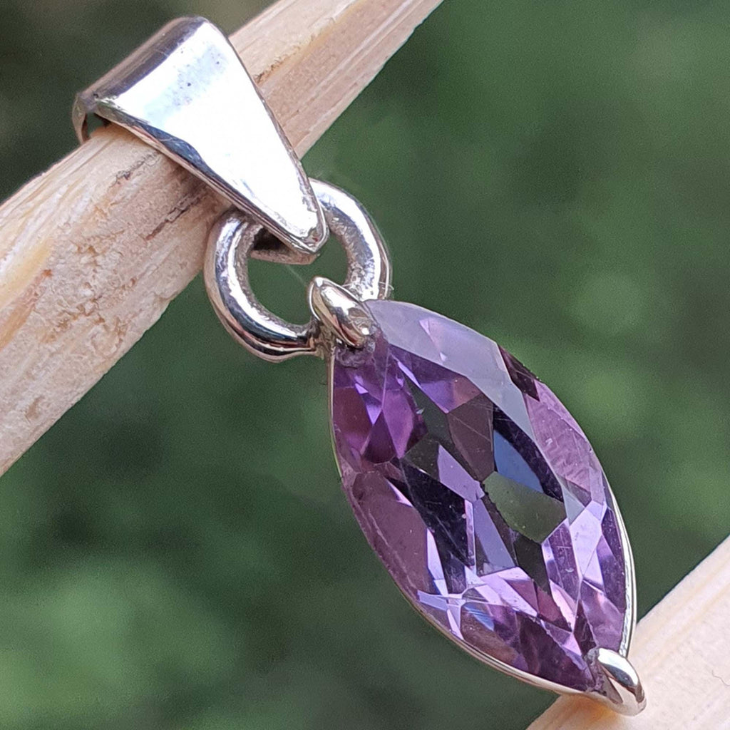 Purple teardrop pendant on a silver chain against a blurred green background