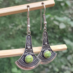 Pair of silver earrings with green stones on a wooden stick against a blurred green background