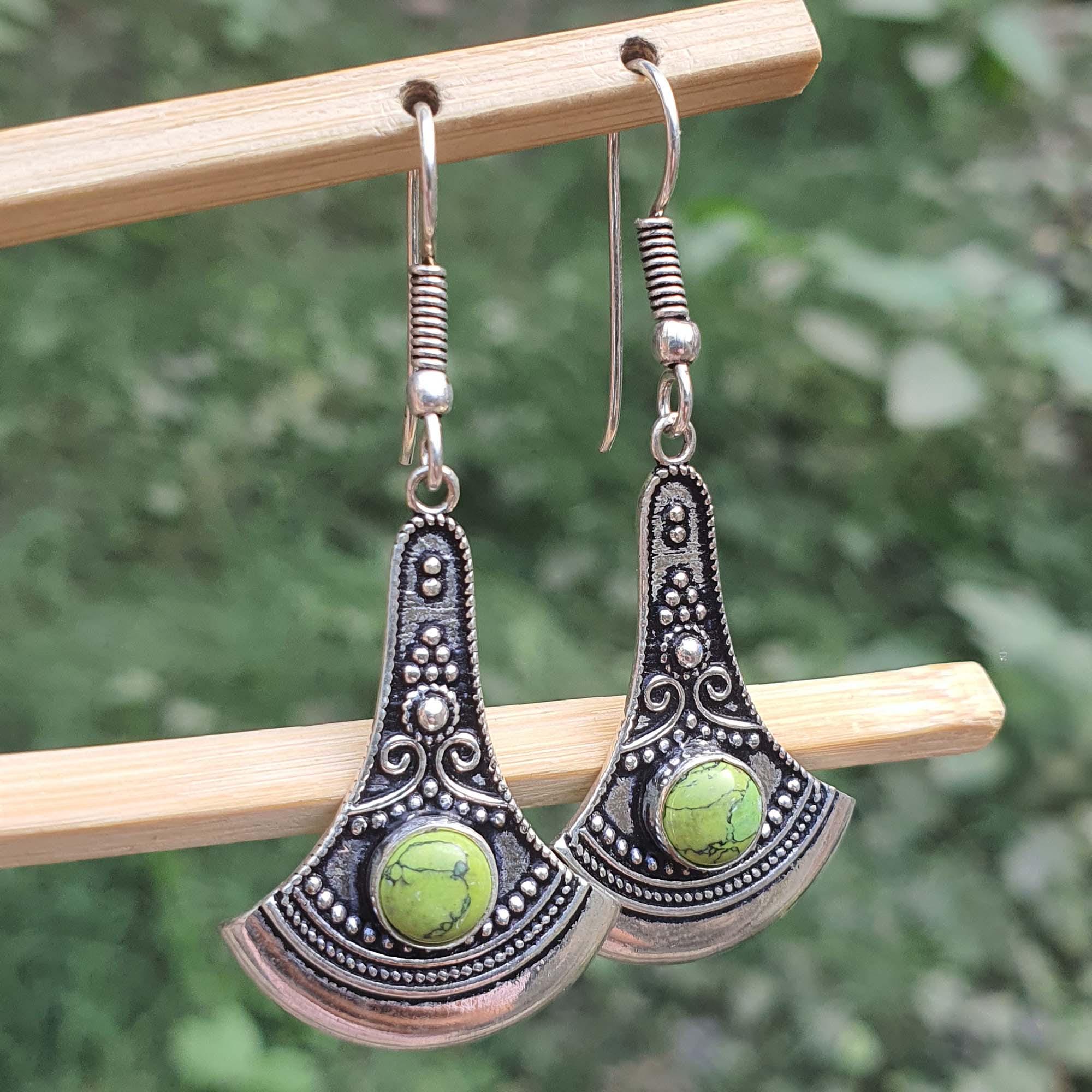 Pair of silver earrings with green stones on a wooden stick against a blurred green background