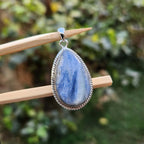 Blue stone pendant on a stick with a blurred green background