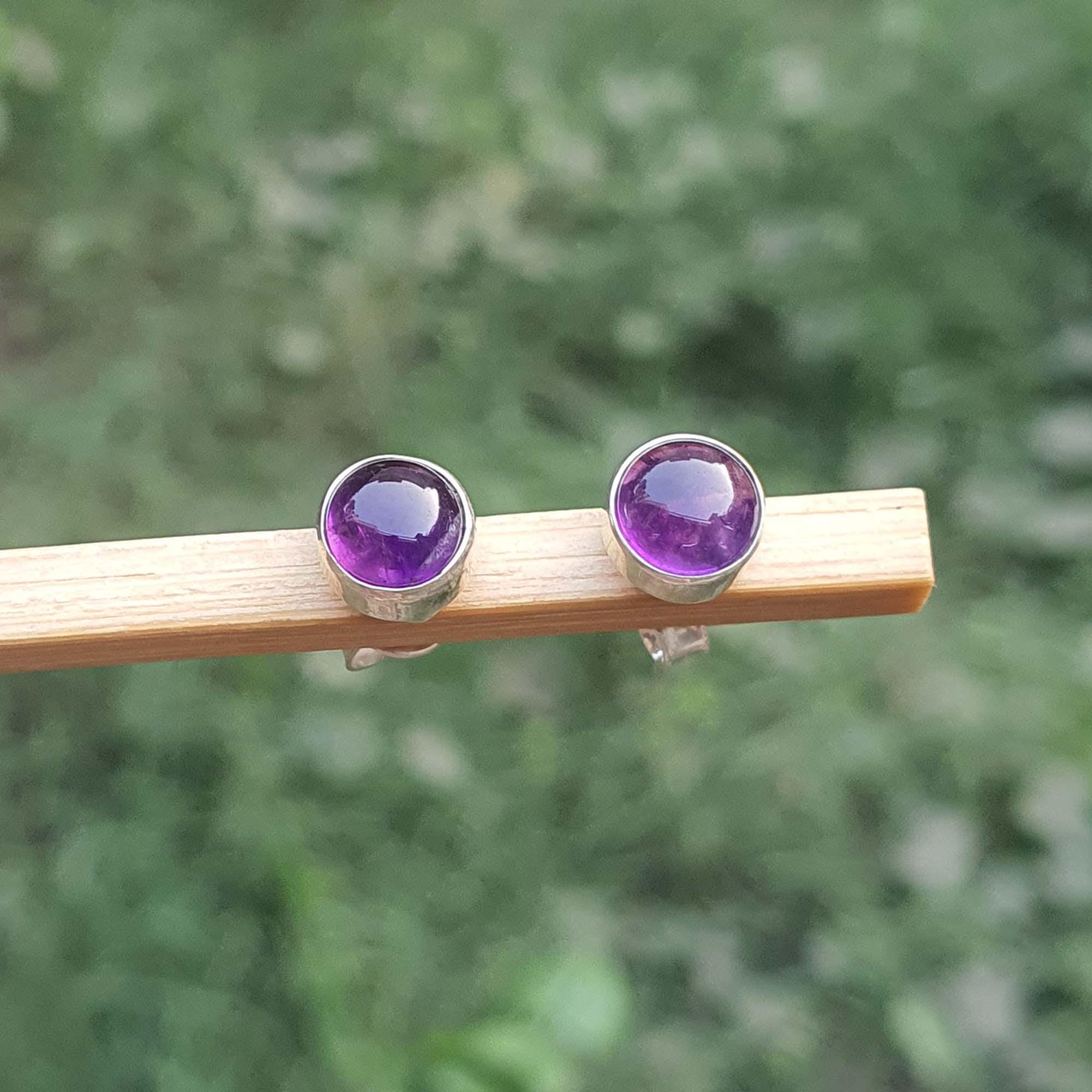 Amethyst stud earrings on a wooden stick with a blurred green background