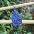 Teardrop-shaped blue pendant on a silver chain against a blurred green background