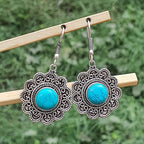 Pair of ornate earrings with turquoise stones on a wooden stick against a blurred green background