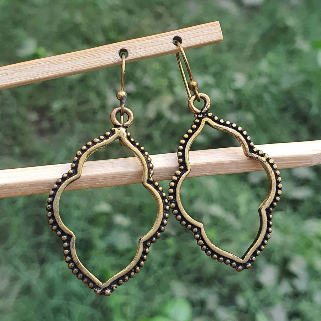 Pair of gold earrings hanging on a wooden stick with a green blurred background