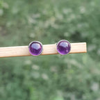 Pair of purple gemstone stud earrings on a wooden stick with a blurred green background