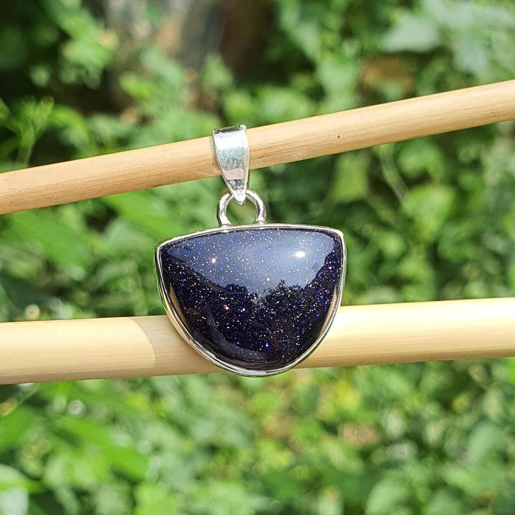 Blue stone pendant on a silver chain held by a wooden stick against a green leafy background