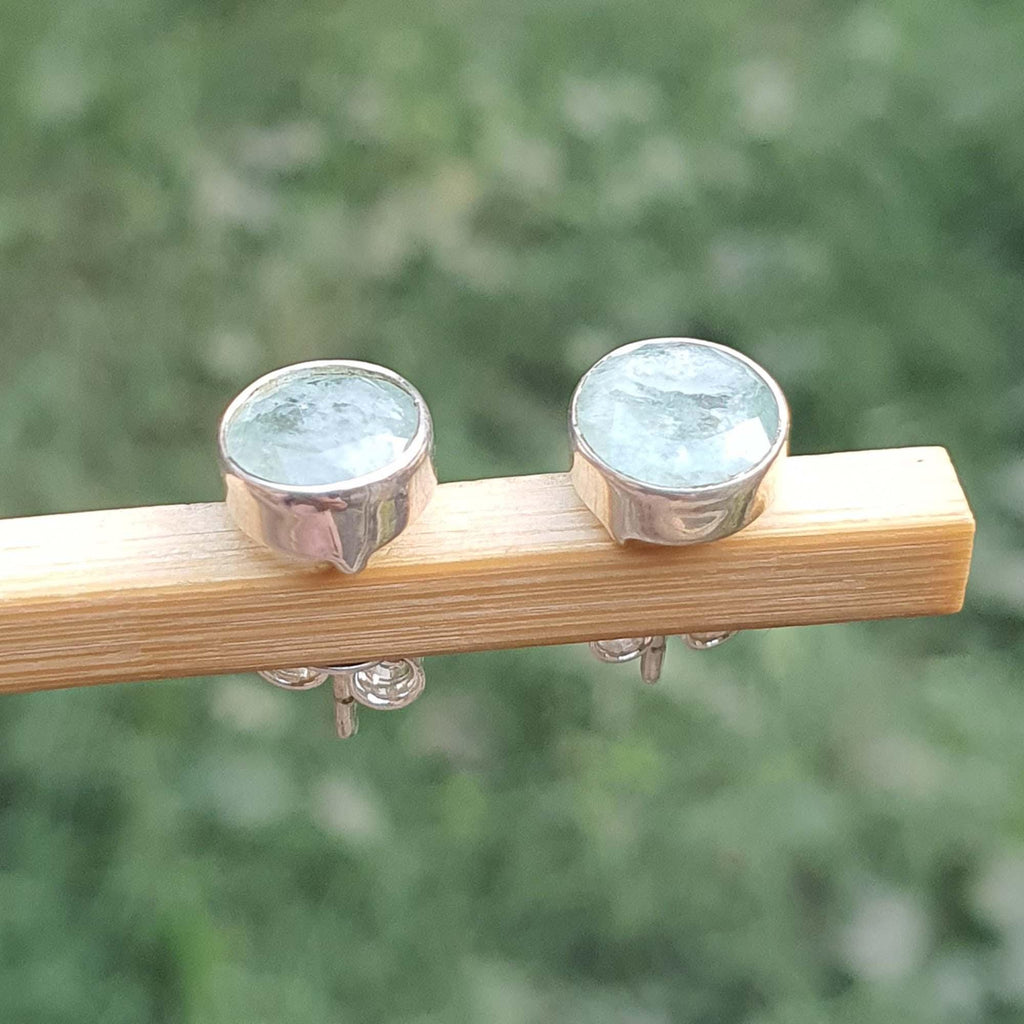 Silver earrings with green gemstones on a wooden stick against a blurred green background