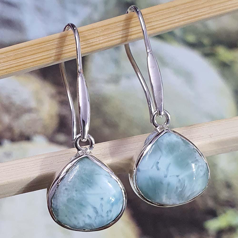 Teardrop-shaped earrings with light blue stones on a wooden stick