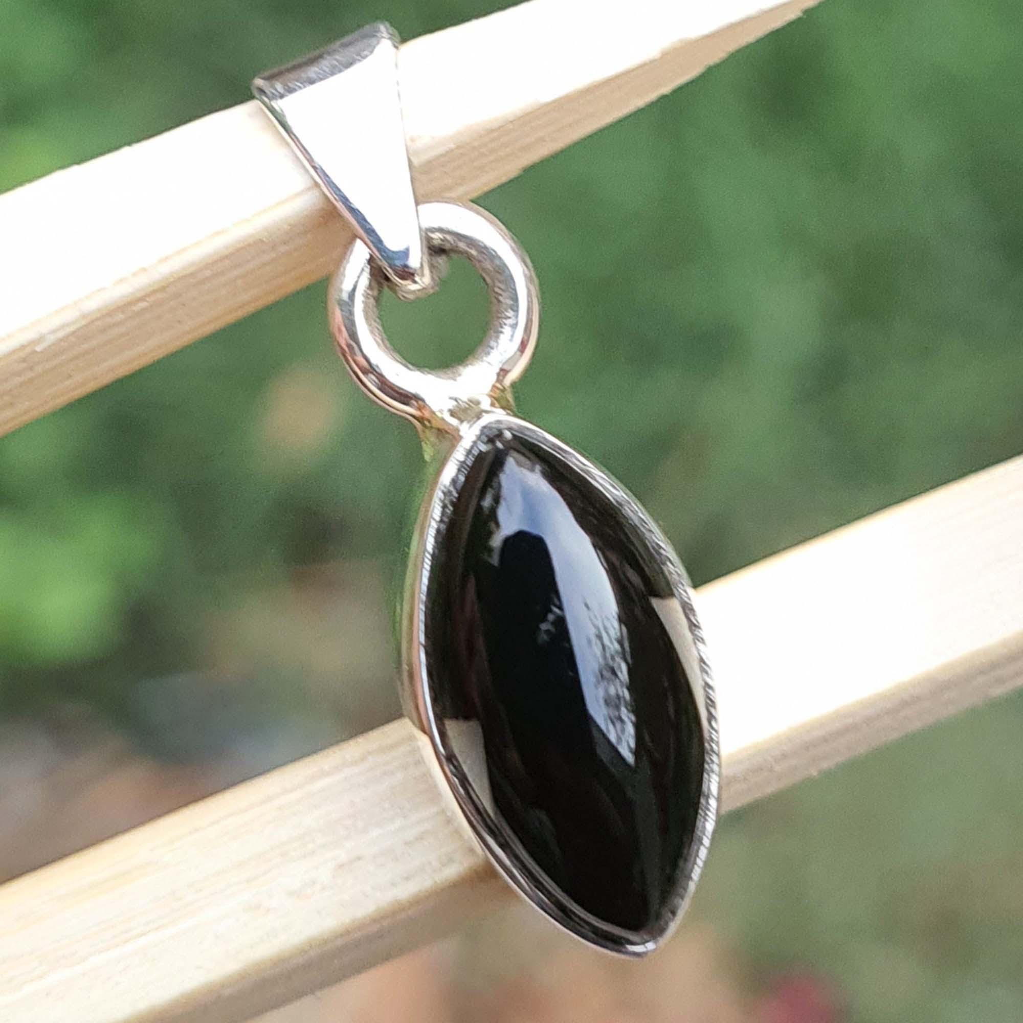 Black teardrop pendant on a silver chain against a blurred natural background