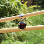 Round pendant with a red heart design on a wooden stick against a green outdoor background